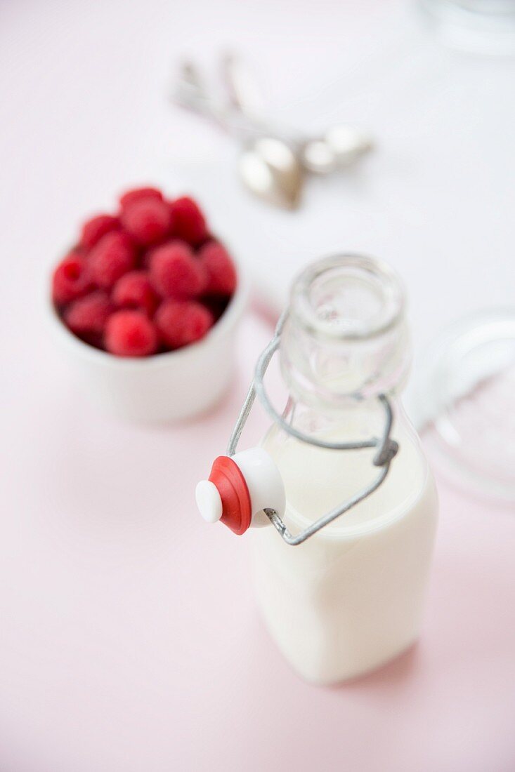 A bottle of milk and raspberries in a white bowl
