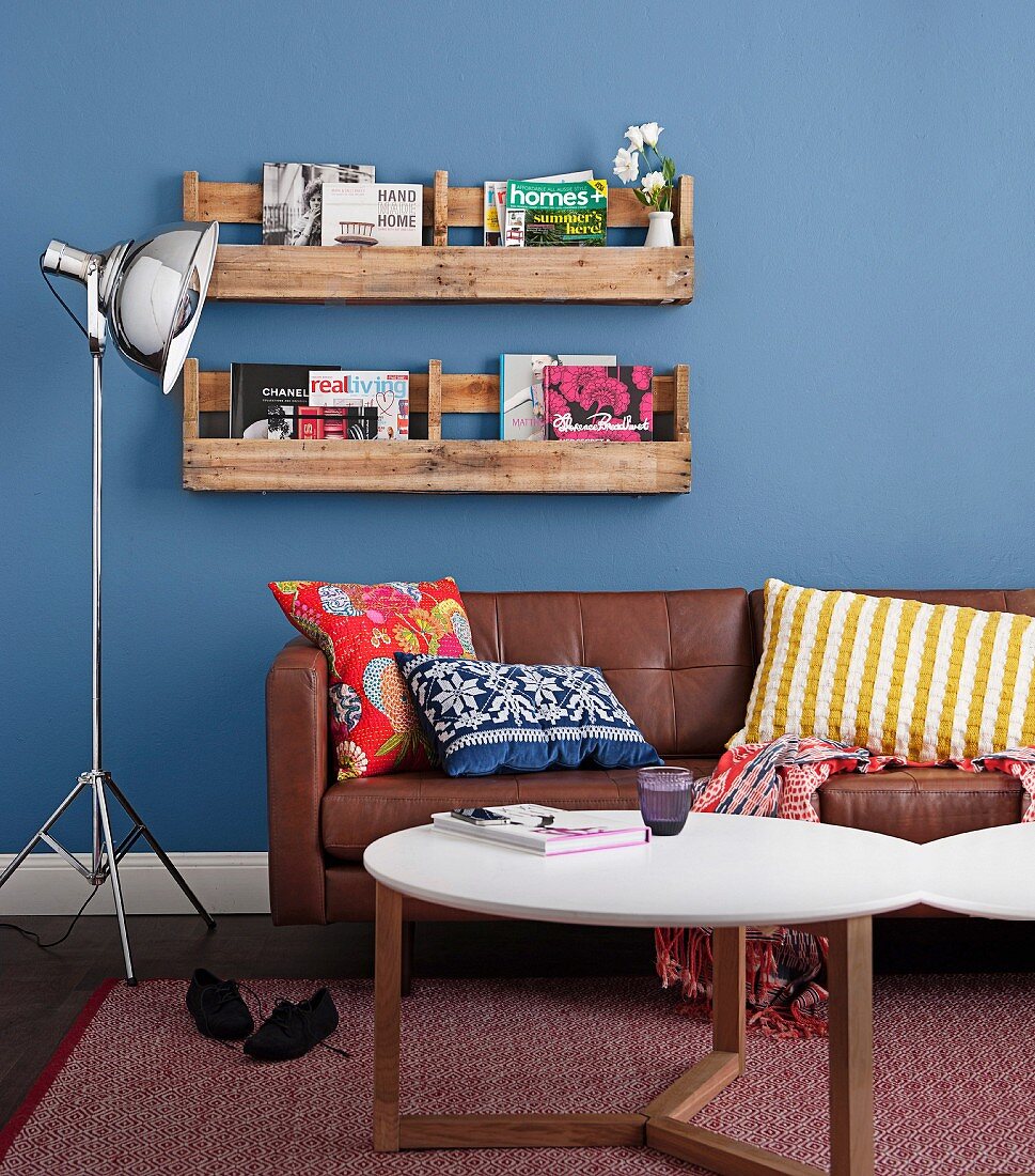 Bookshelf made of sawn-up pallets on a blue wall above a leather sofa