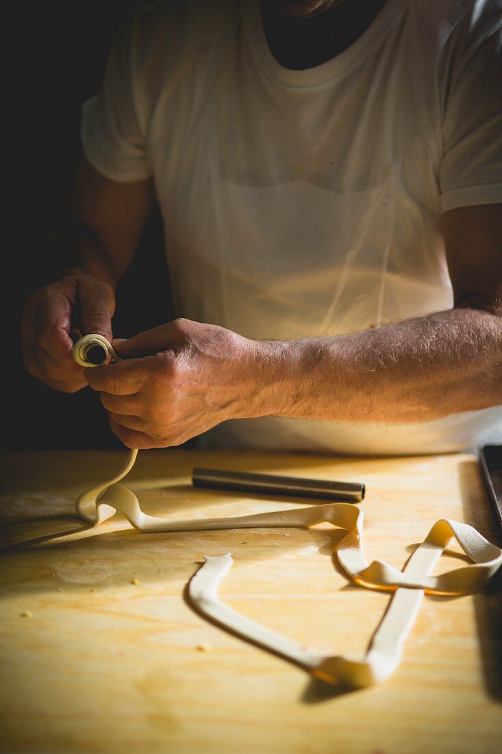 A confectioner rolling a strip of pastry around a metal stick