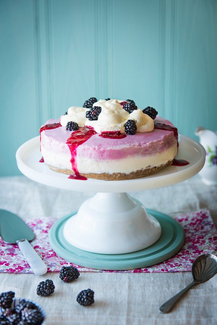 Blackberry cheesecake on a cake stand with cream and fresh blackberries