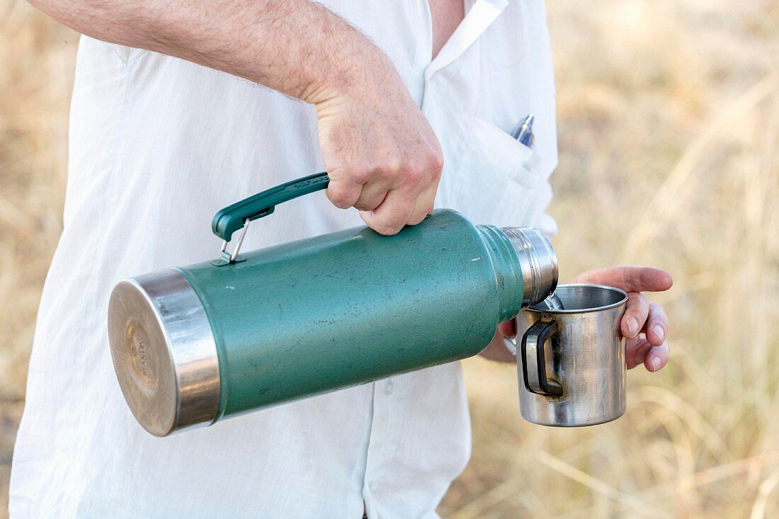 Tea being poured from a Thermos flask into a tin mug