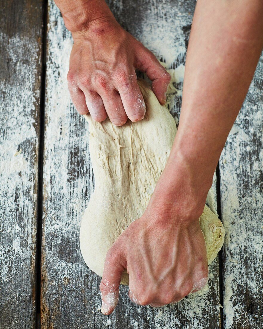 Bäcker knetet Teig auf bemehlter Holzoberfläche