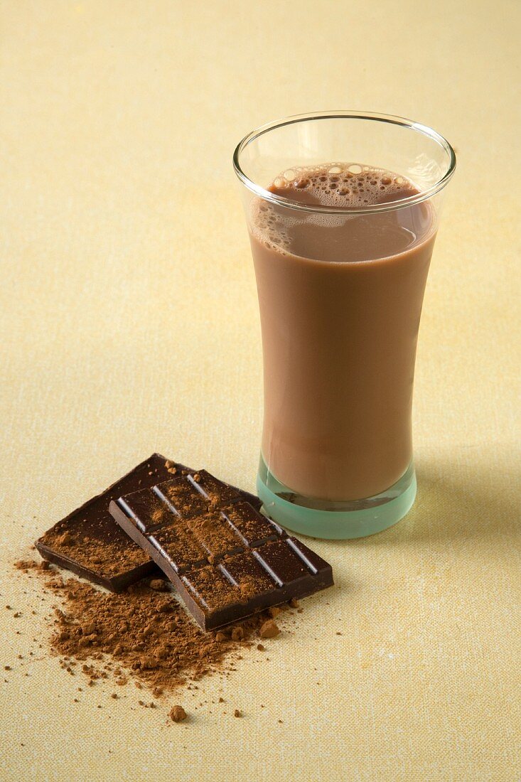Schokoladenmilch im Glas, daneben Schokolade und Kakaopulver