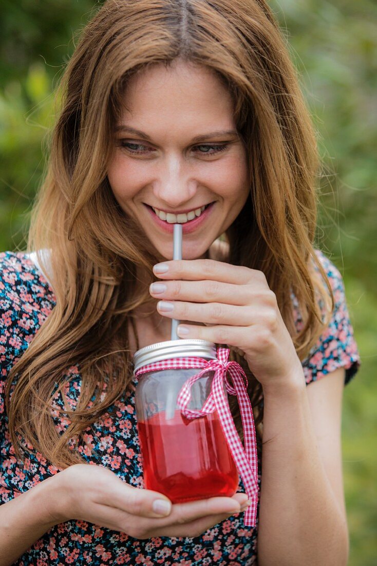 A woman drinking iced tea from a screw-top jar with a straw