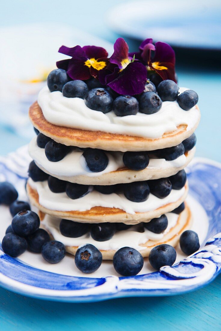 A stack of pancakes with blueberries and pansies
