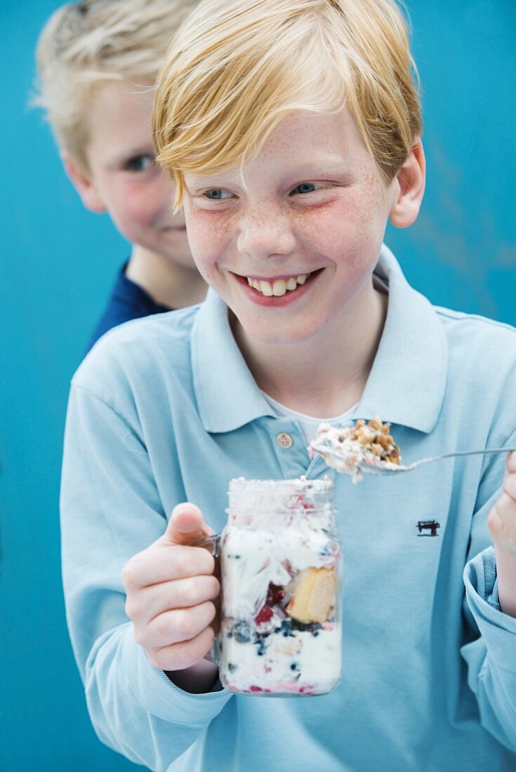 A boy eating yoghurt muesli with berries from a glass