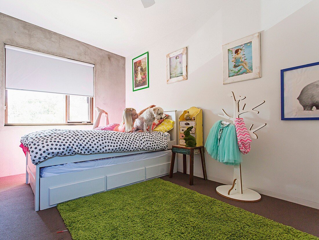 Girl with dog on bed in children's room with concrete wall and flea market items