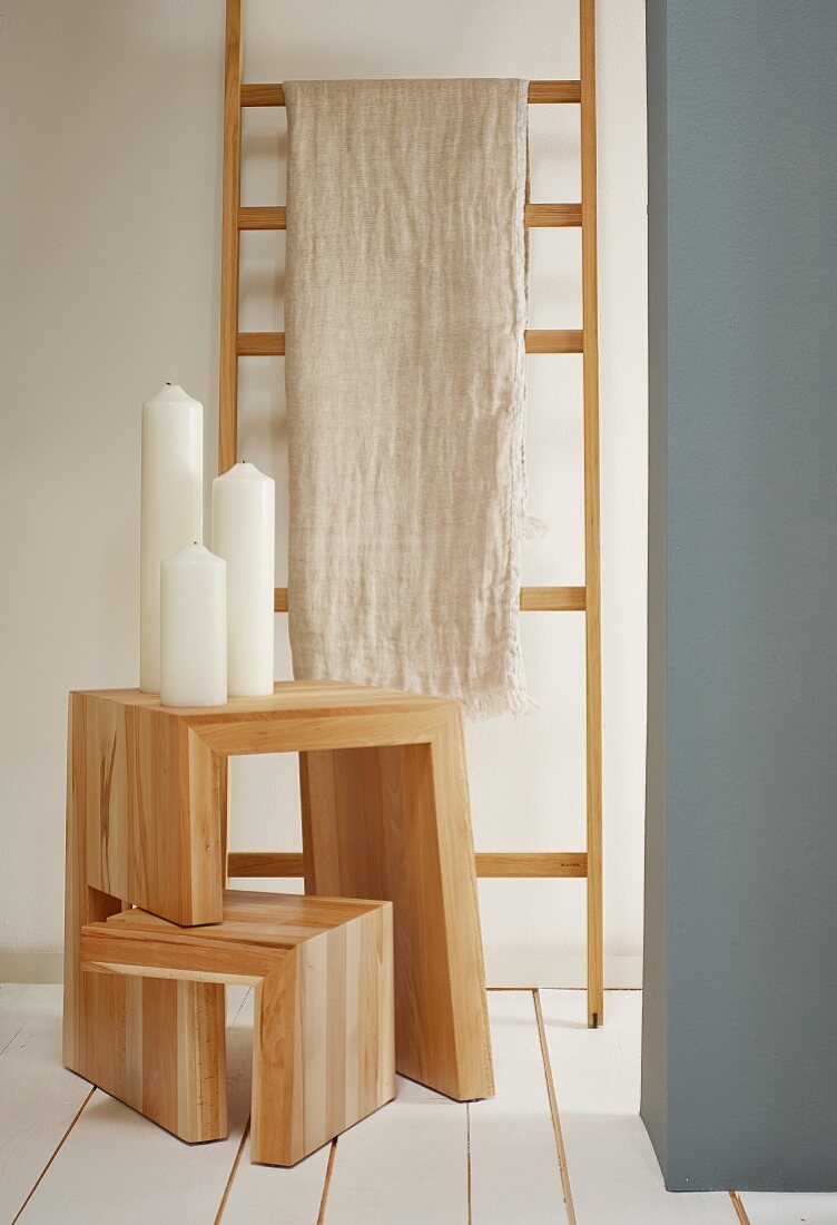 Linen cloth hung over wooden ladder used as clothes rack and pillar candles on adjustable wooden stool