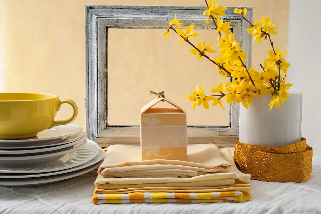 Gestapelte weiße Teller, gelbe Tasse und Tischwäsche, Forsythienzweige in Vase