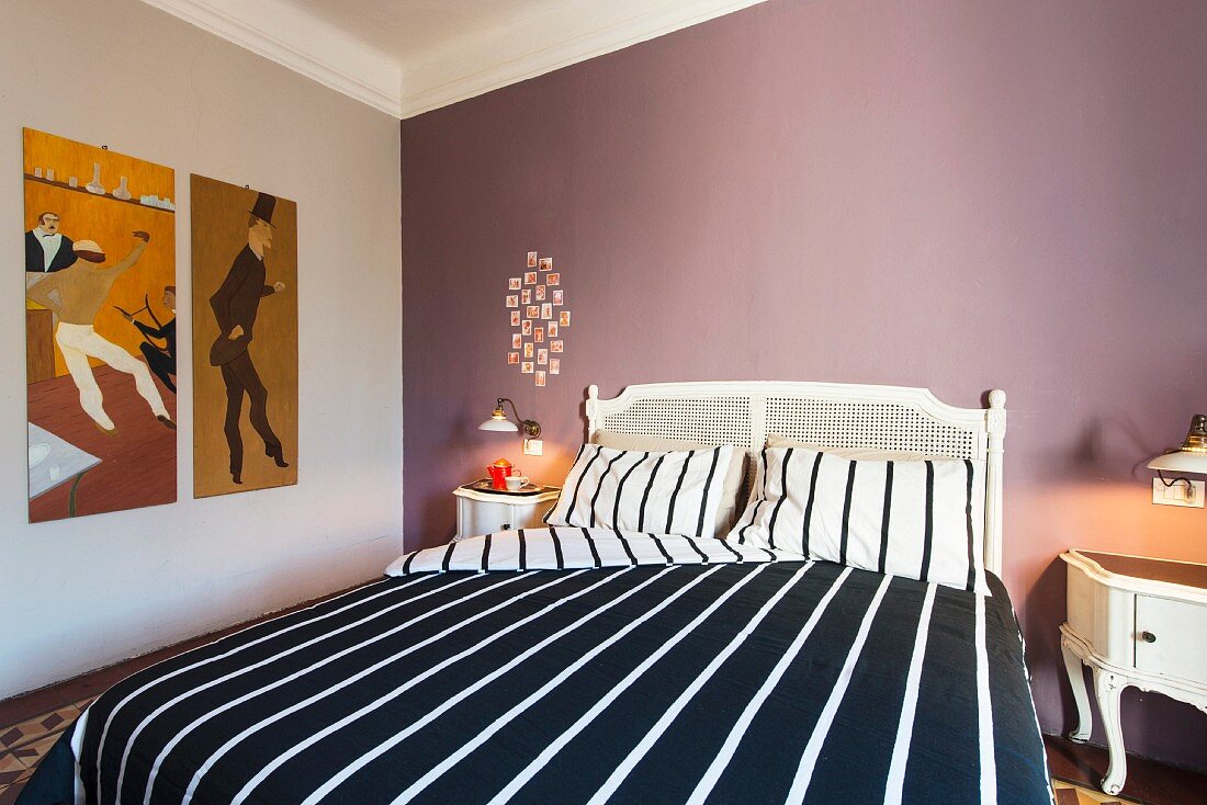 Weisses Doppelbett mit schwarz-weiss gestreifter Bettwäsche vor mauvefarbener Wand