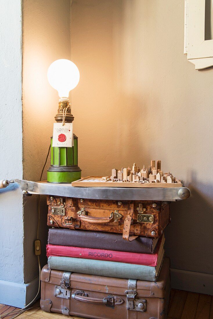 Table lamp and architectural model on surface on top of stacked vintage suitcases and books
