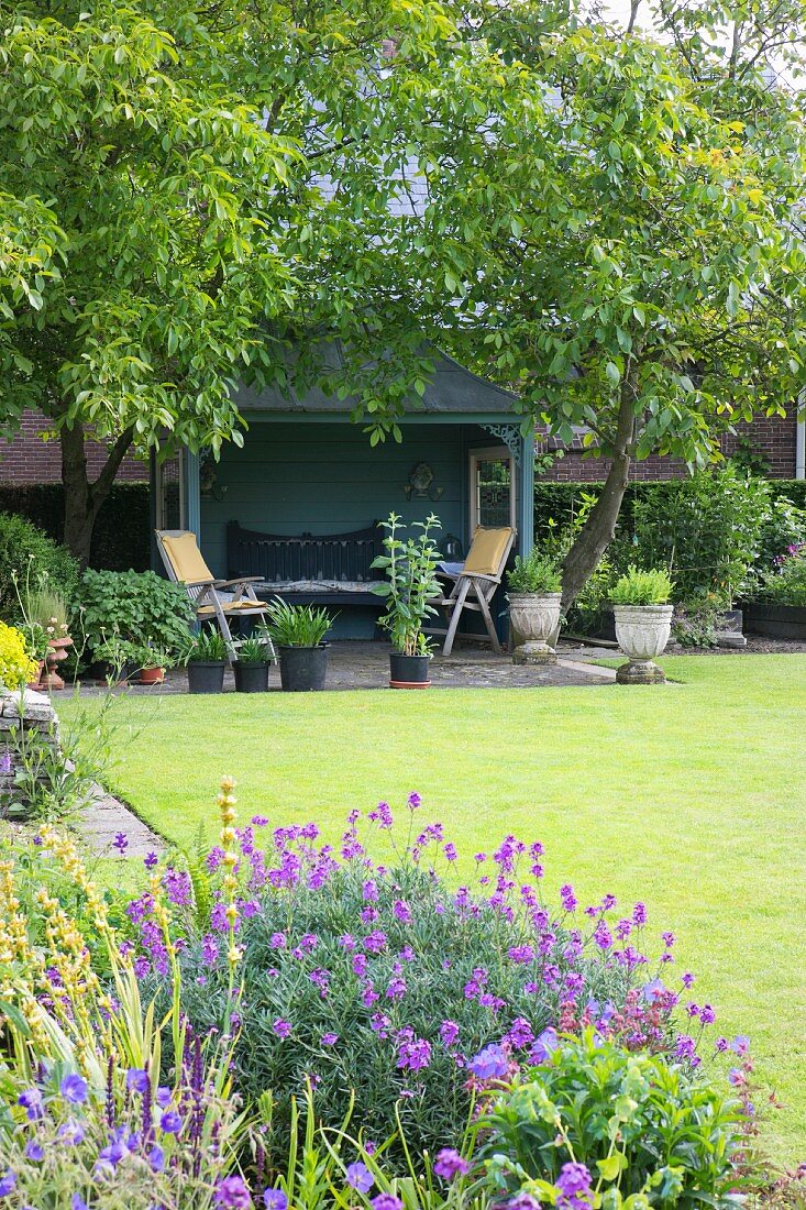 Violettblühende Stauden und gemähte Rasenfläche vor Pavillon im Garten