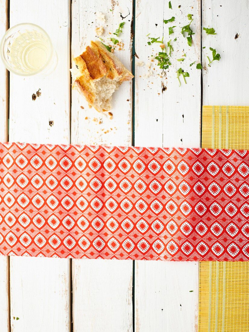 Pieces of bread and white wine on a white wooden table with a patterned napkin