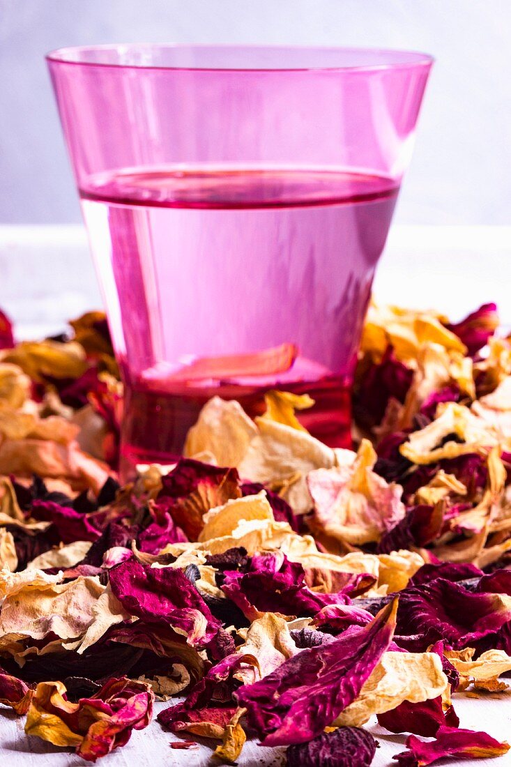 A close-up of a glass of rose water and dried rose petals