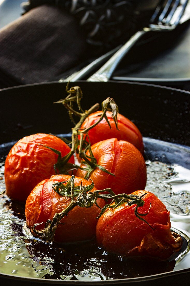 Oven-roasted tomatoes in a black iron pan with a fabric napkin and cutlery in the background
