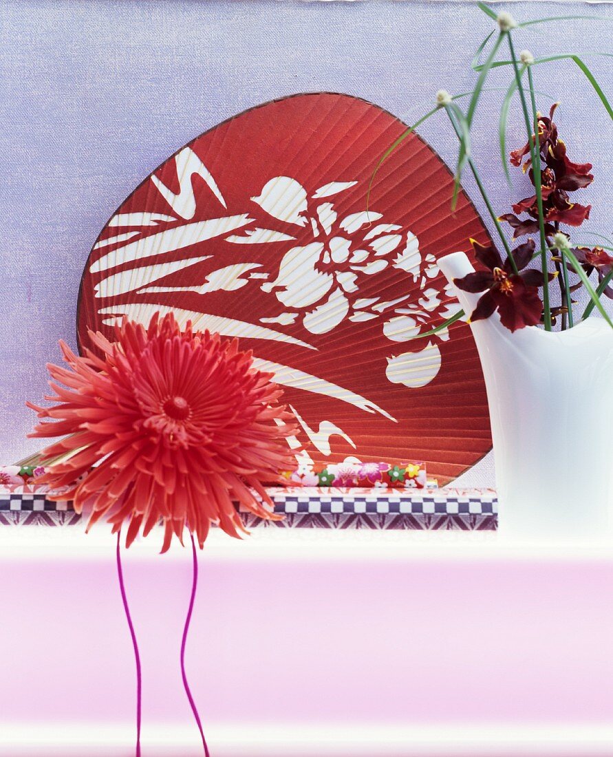 Artificial flower in front of red Oriental fan and orchid