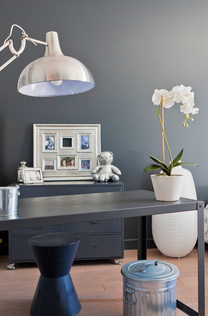 Schreibtisch aus Metall mit einer Orchidee vor grauer Wand