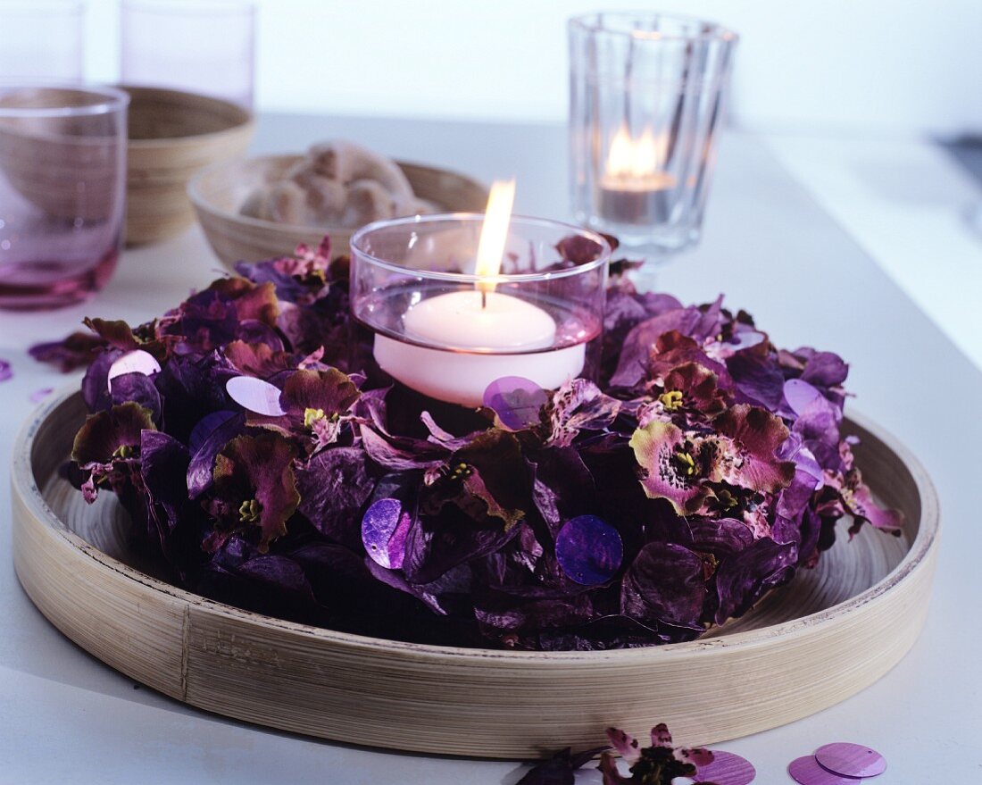 Lit, white floating candle in wreath of purple pot pourri