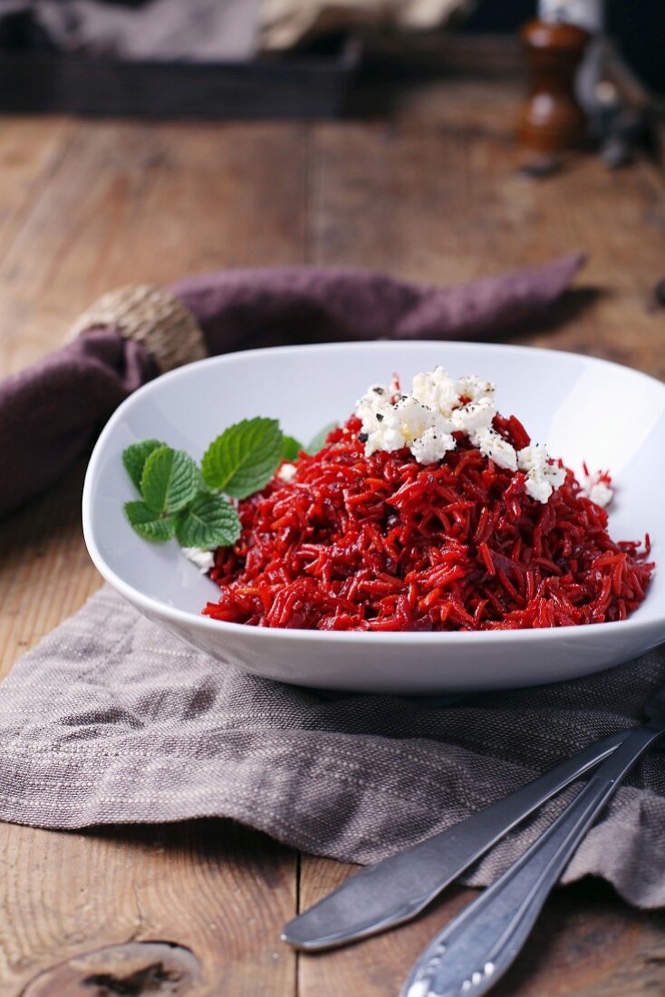 Beetroot risotto with feta cheese and mint in a white bowl on a wooden table