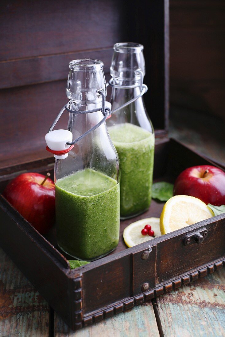 Spinach and banana smoothies in bottles in a wooden crate