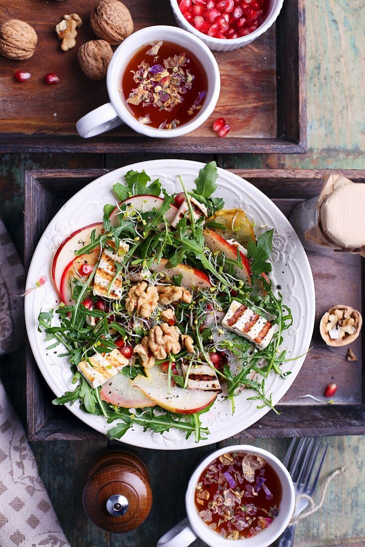 Rocket fired with walnuts and grilled tofu with cups of tea and pomegranate seeds