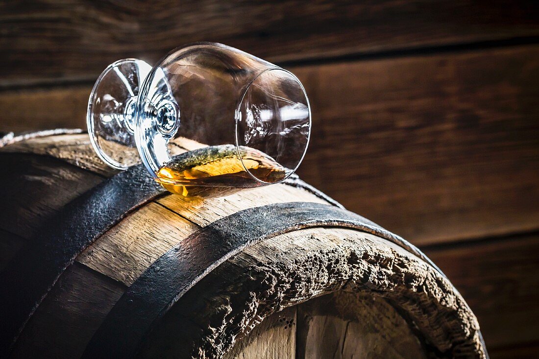 Umgekipptes Glas Cognac auf einem alten Holzfass
