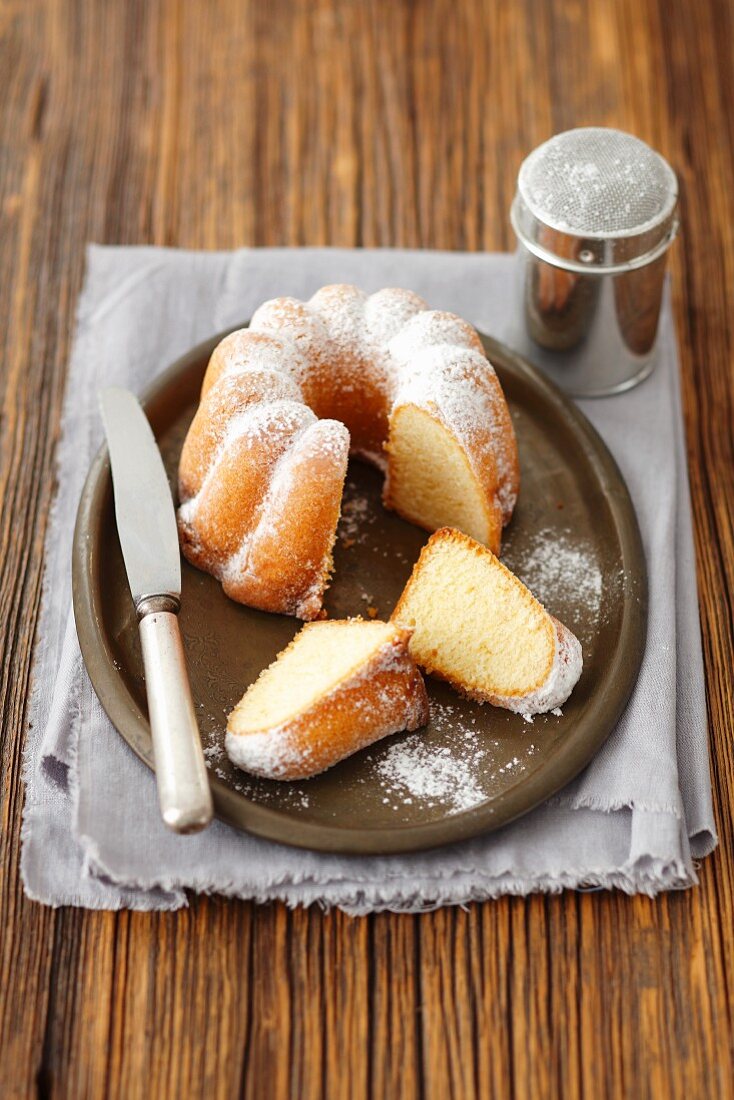 Lemon cake dusted with icing sugar, with a slice cut