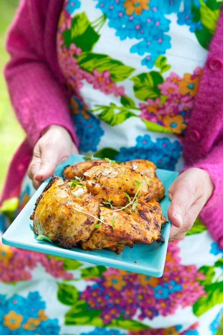 A woman holding a platter of grilled chicken