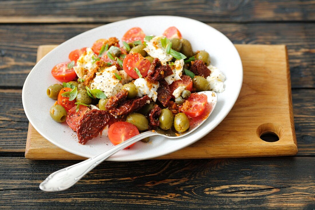 Salat mit Kirschtomaten, getrockneten Tomaten, Mozzarella, Oliven und Basilikum
