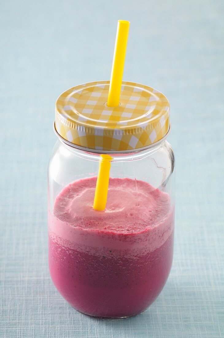 A beetroot smoothie in a screw-top jar with a straw