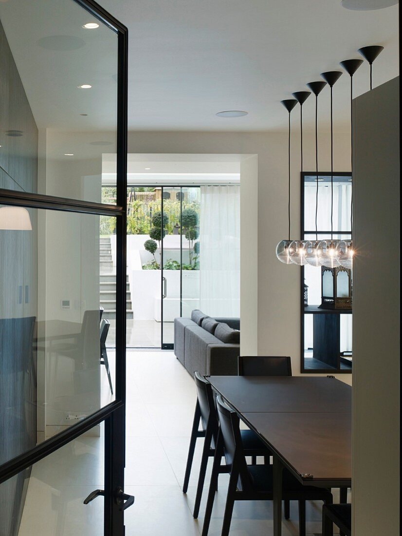 View of black dining table, living room and terrace garden through open glass door