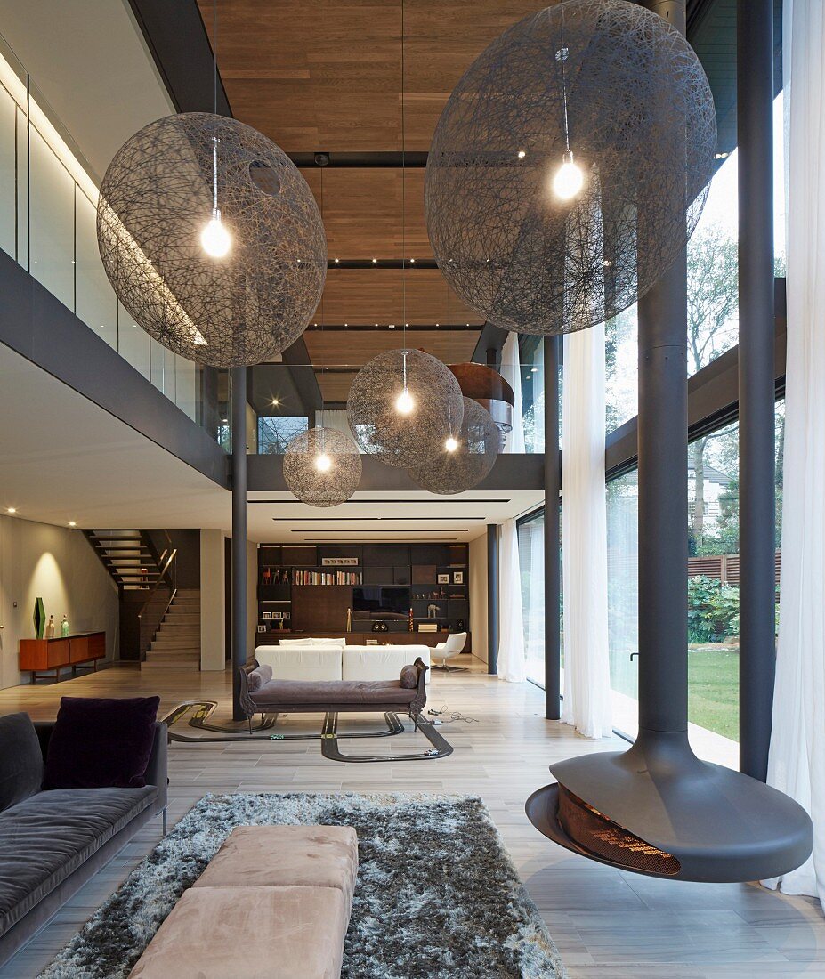 Huge spherical lamps and suspended fireplace in futuristic, double-height living room
