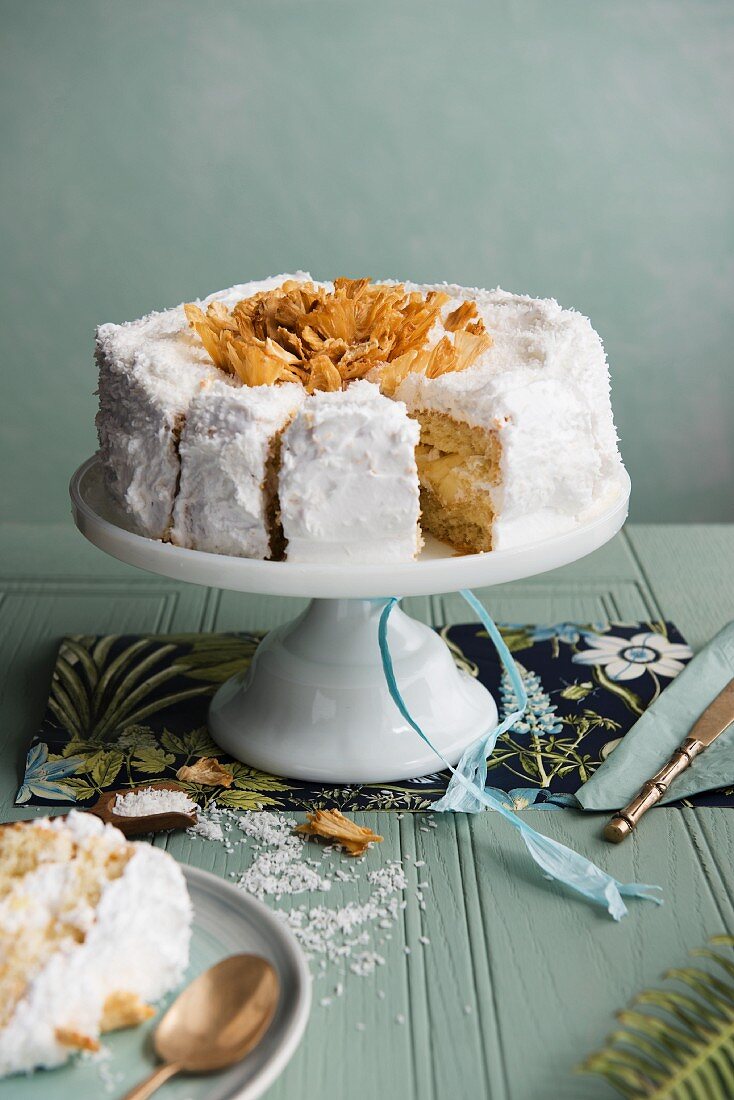 A whole coconut and pinapple cake on a cake stand, sliced
