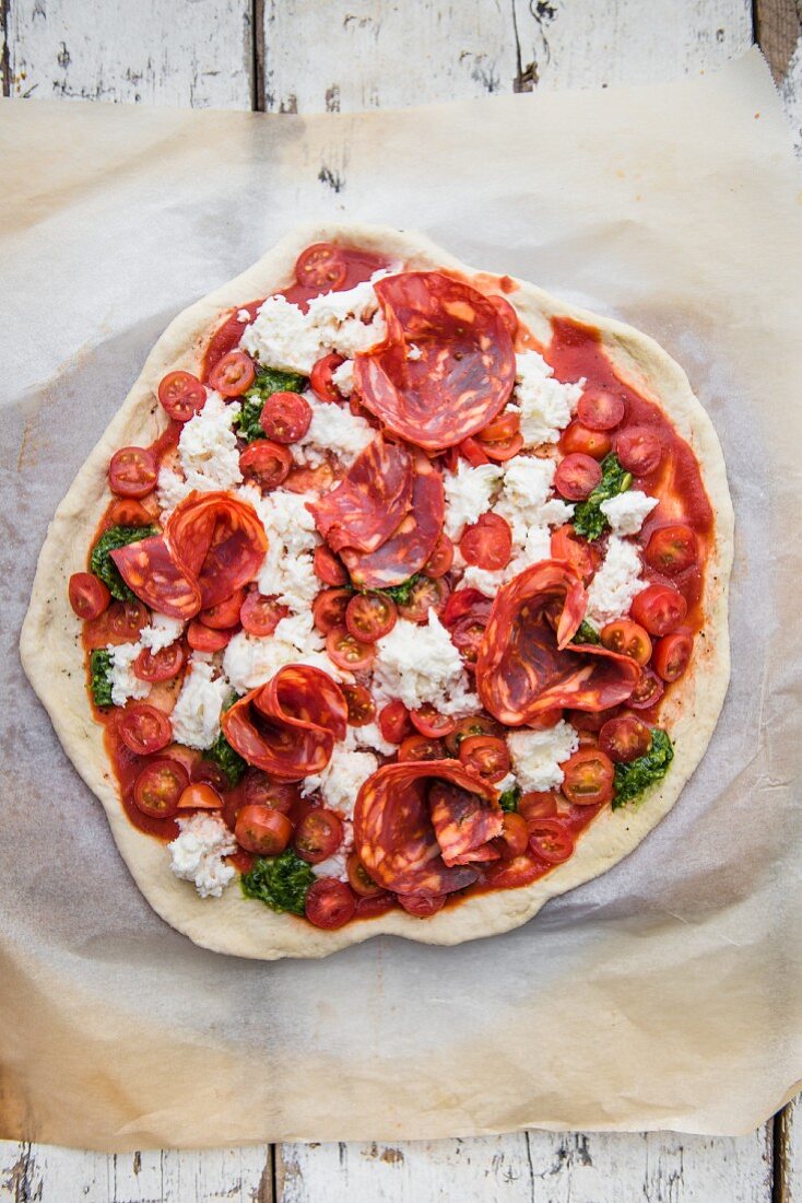 An unbaked pizza with tomatoes and salami