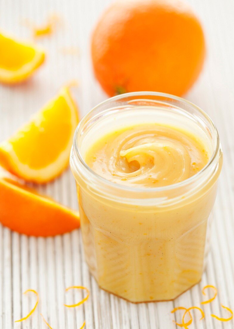 Ein Glas Orangen-Karamell-Aufstrich mit Orangenzesten und frischen Orangen