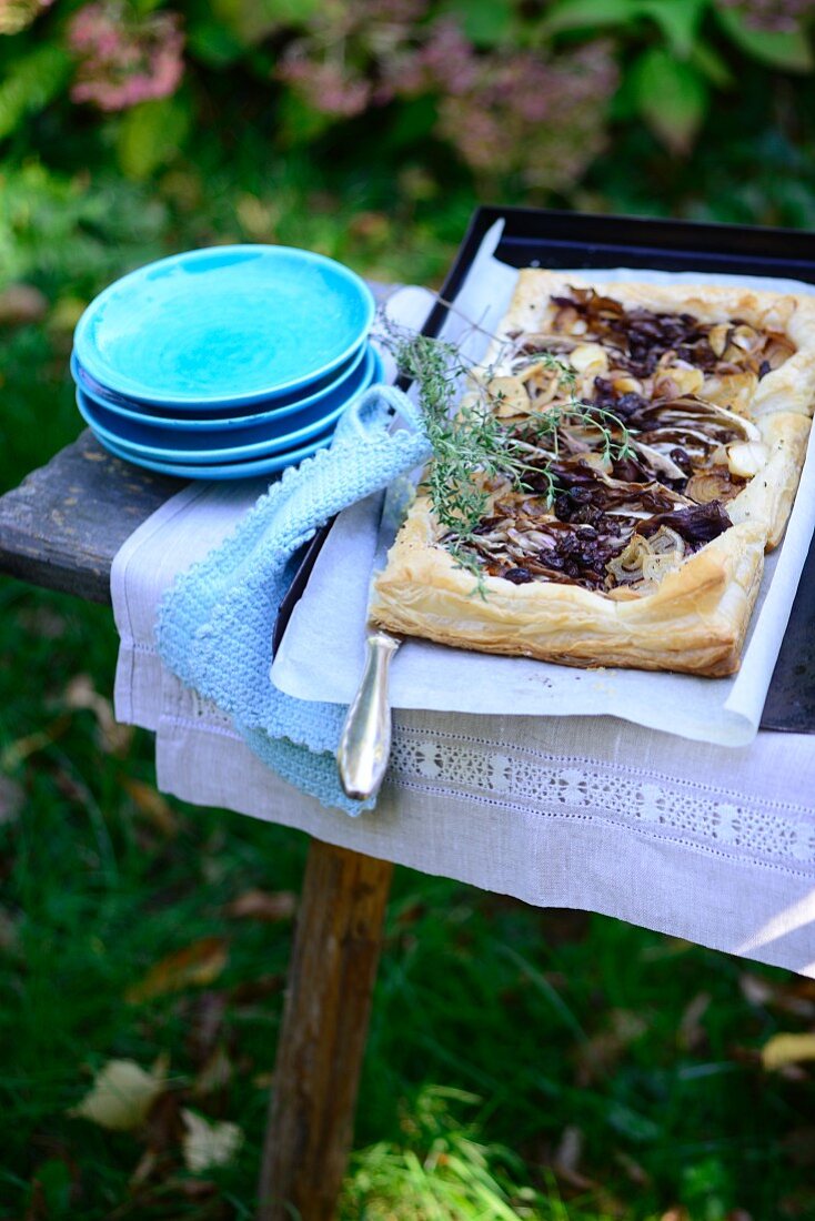 A puff pastry tart with braised radicchio and shallots on a table in a garden
