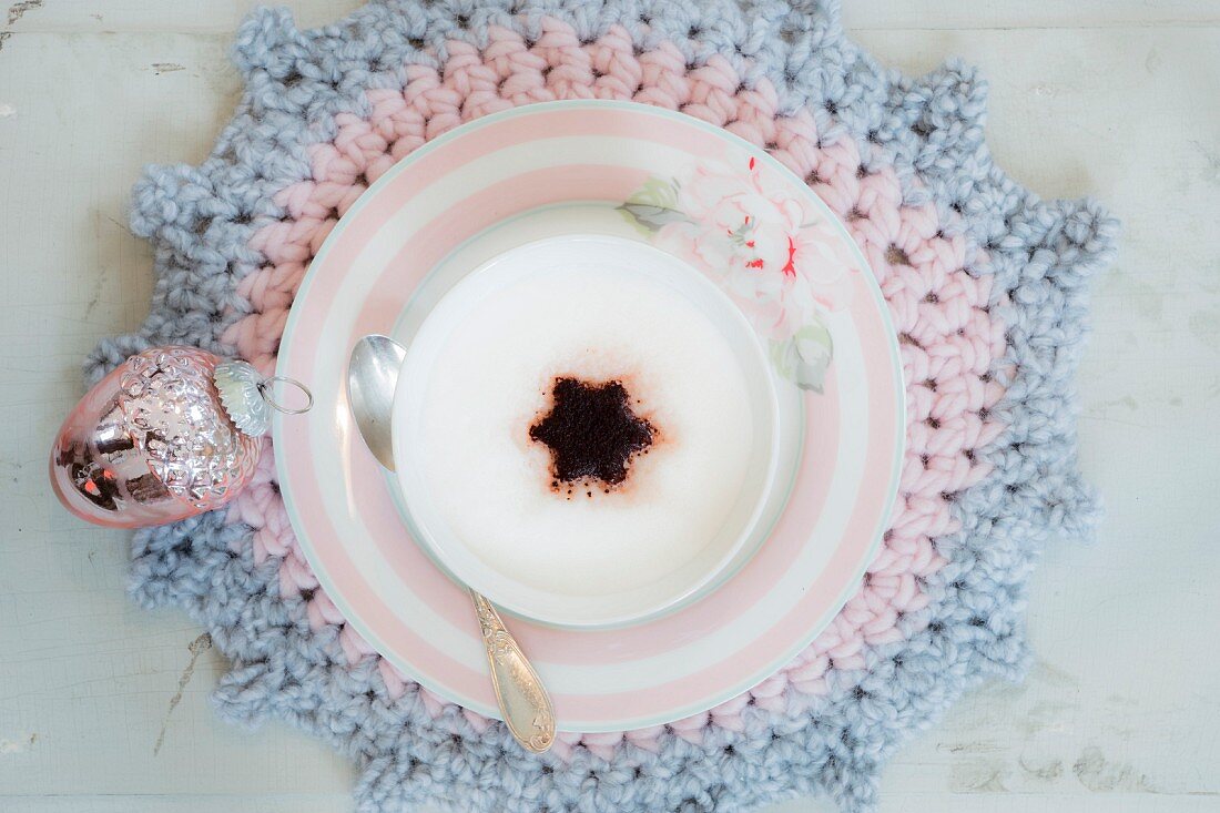 Eine Tasse Cappucchino auf einem gehäkelten Platzteller