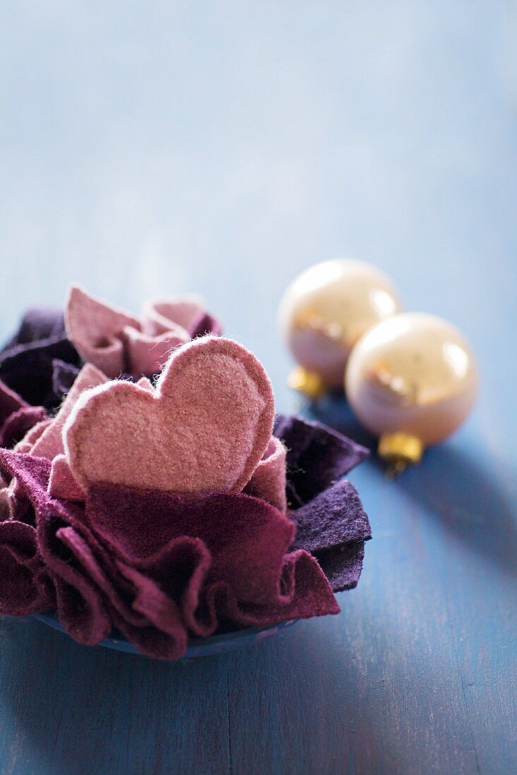 Felt love-heart and pieces of felt in bowl next to Christmas-tree baubles