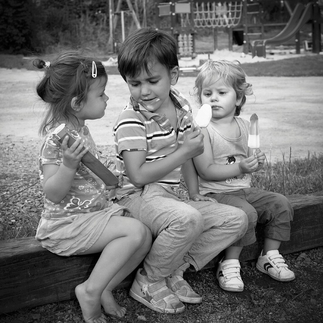 Three children eating ice cream in playground (black and white photo)