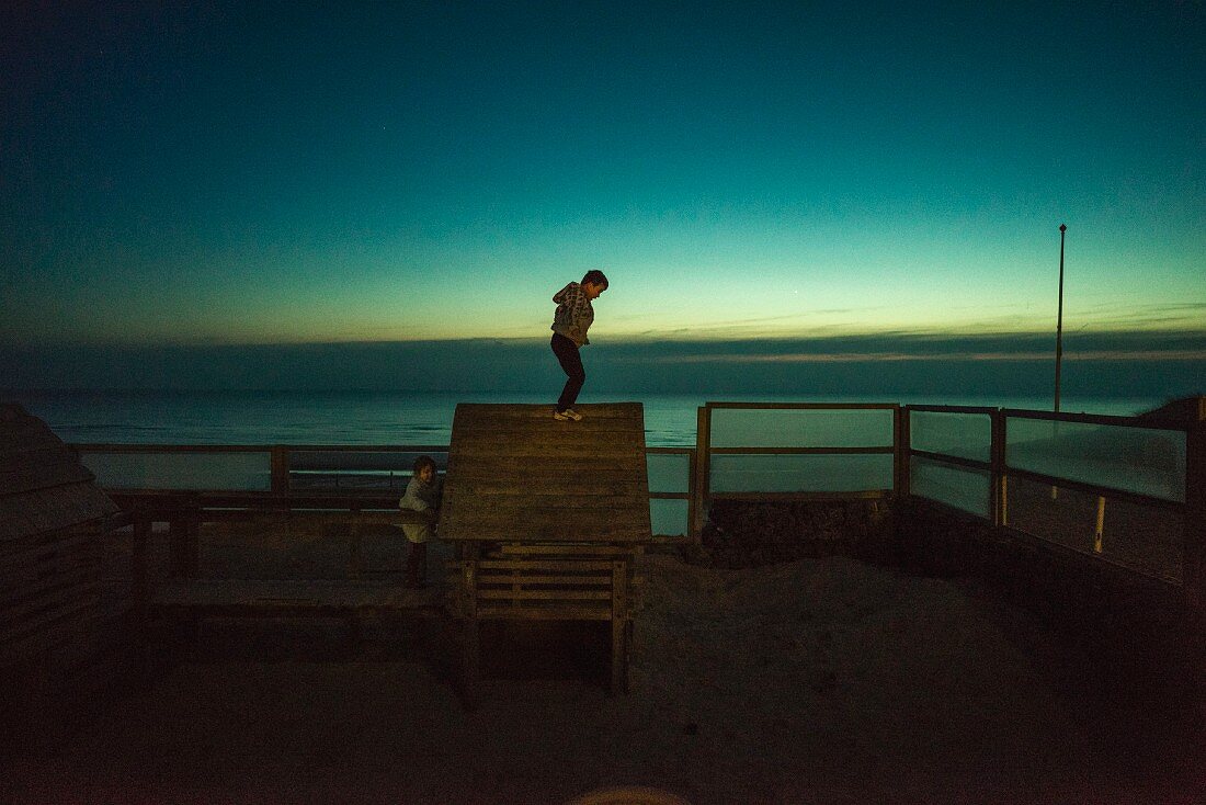 Little boy standing on top of wooden hut at dusk