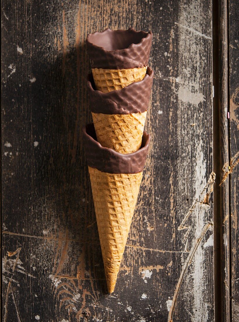 A stack of three chocolate dipped ice cream cones on a wooden surface