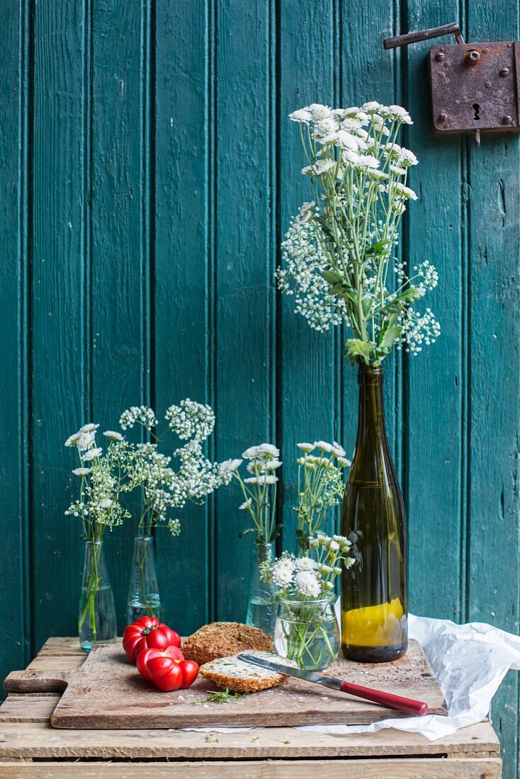 Bread with herb butter and tomatoes next to white flowers in front of an old wooden door