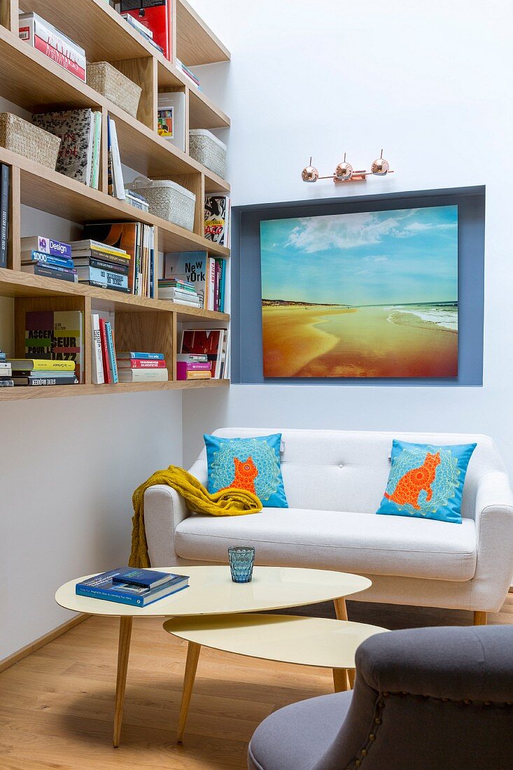 Sofa and retro tables below wooden wall-mounted shelving and artwork in niche