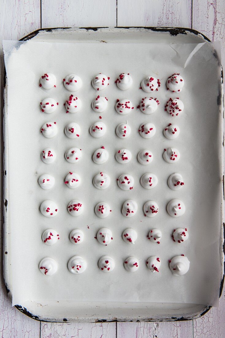 Mini meringues decorated with dried raspberries on baking paper (seen from above)