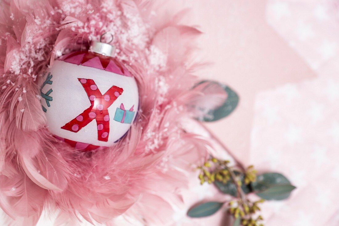 Painted Christmas bauble surrounded by delicate pink feathers