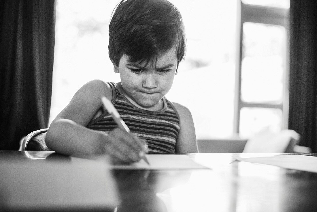 Kleiner Junge schreibt auf Blatt Papier (s/w-Foto)