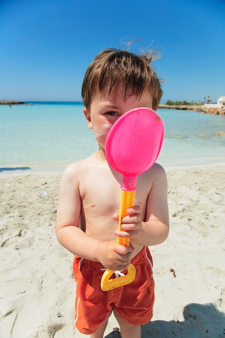 Boy holding spade with sun lotion on face