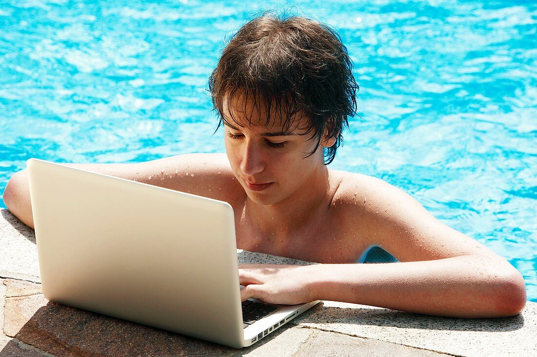 Teenager using a laptop by a pool