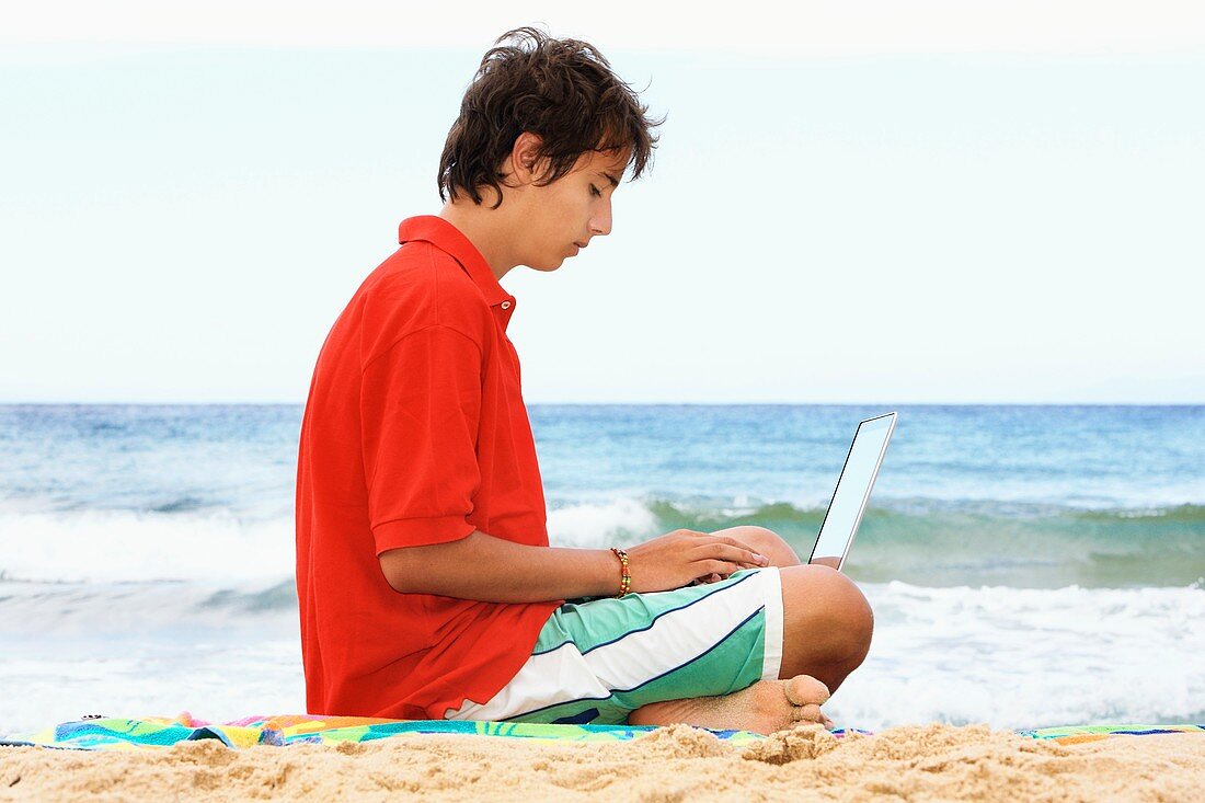 Boy using a laptop at a beach