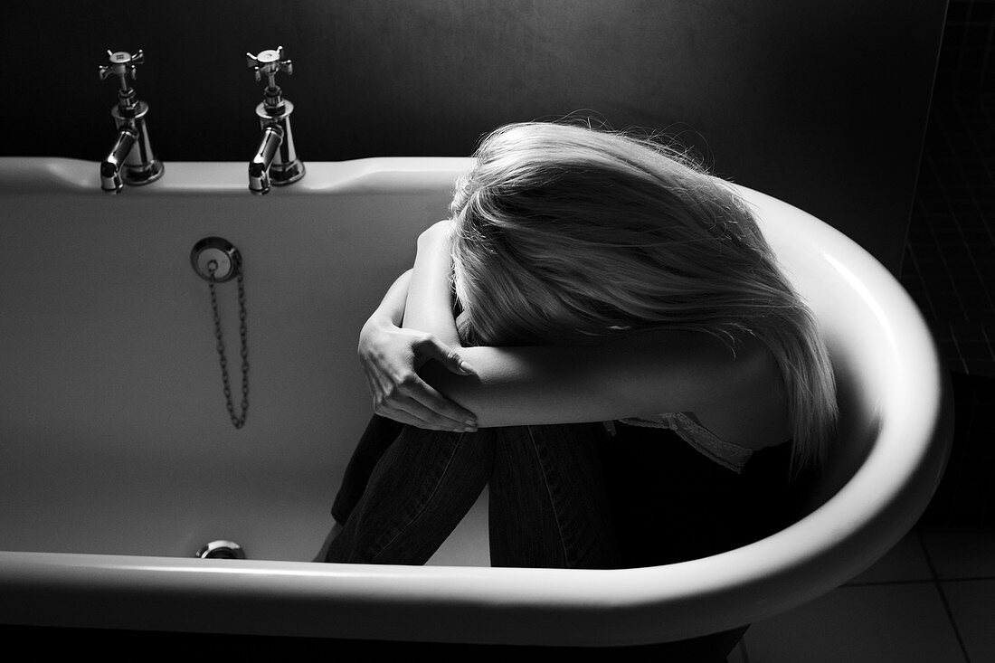 Depressed young woman in an empty bathtub